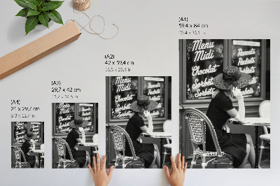 Affiche décorative Une femme portant un chapeau, assise à une table dans un café
